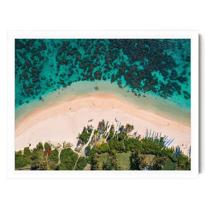 An aerial view of a tropical beach with crystal clear turquoise waters, sandy shores, and lush vegetation surrounding the area.