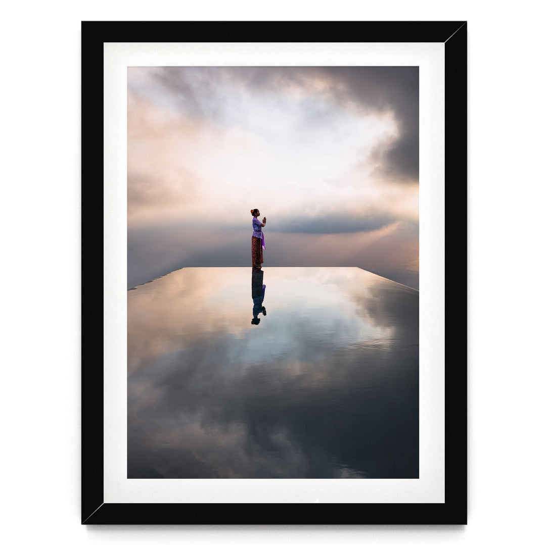 A person stands on a reflective surface, gazing out at the cloudy sky, creating a serene and contemplative scene.