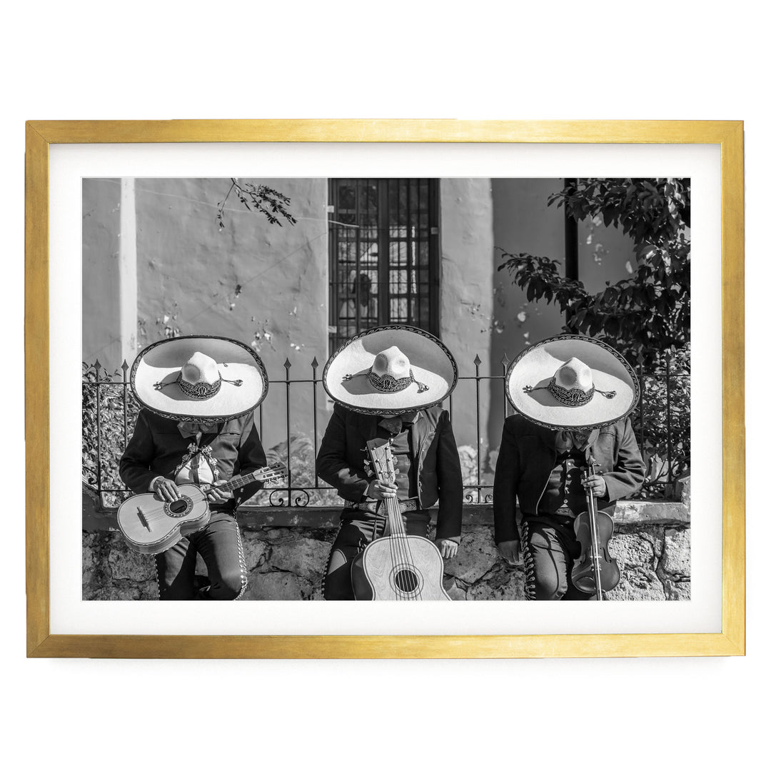 A black and white photograph of three men wearing sombreros and playing musical instruments, such as guitars and drums, in front of a building.