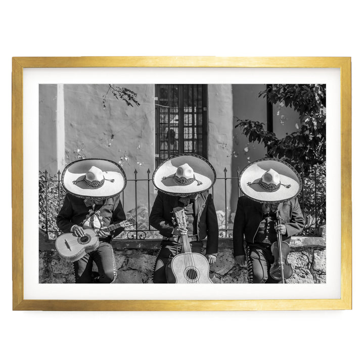 A black and white photograph of three men wearing sombreros and playing musical instruments, such as guitars and drums, in front of a building.
