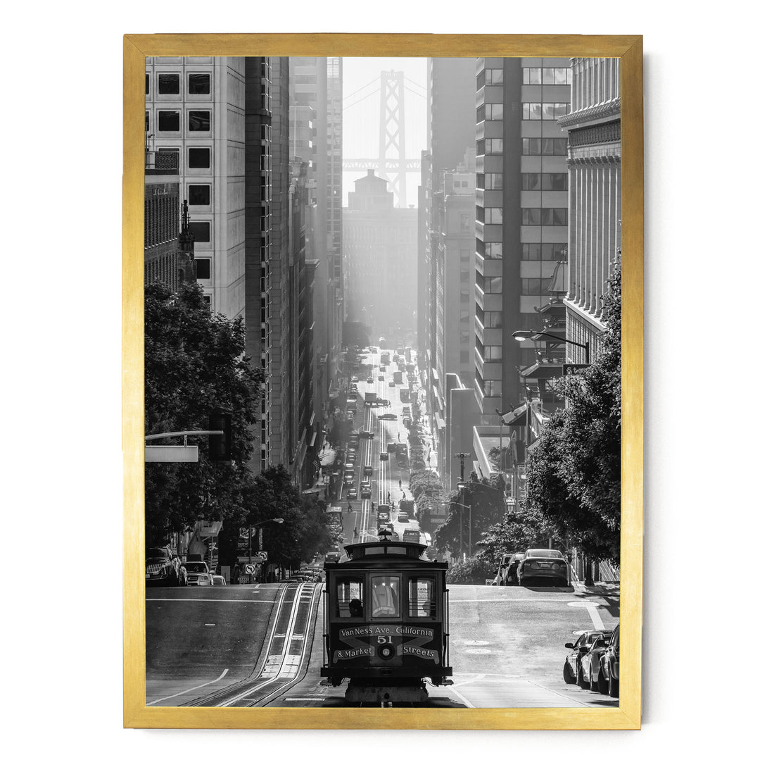 A black and white photograph of a cable car traveling down a busy city street, with tall buildings and a bridge in the background.