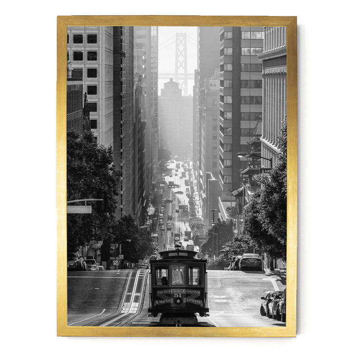 A black and white photograph of a cable car traveling down a busy city street, with tall buildings and a bridge in the background.