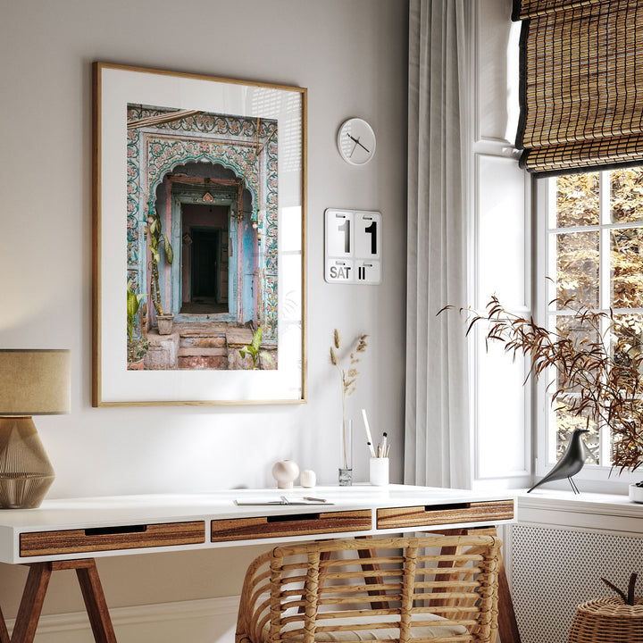 a modern and minimalist living space with a large framed picture of an ornate doorway on the wall, a white desk with a lamp and a plant, and a window with a bird perched on the sill.