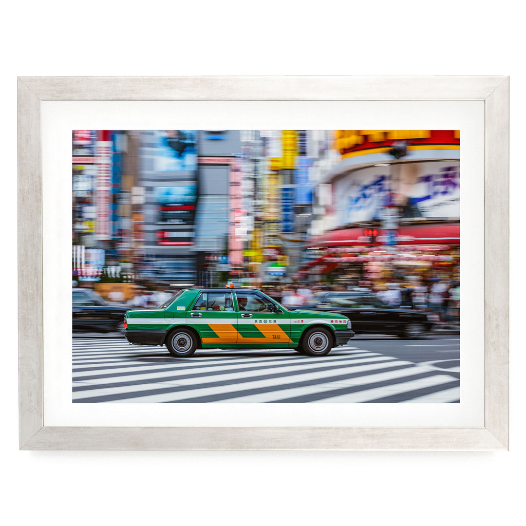 A green taxi cab is captured in motion, driving through a busy city street lined with colorful buildings and blurred pedestrians.