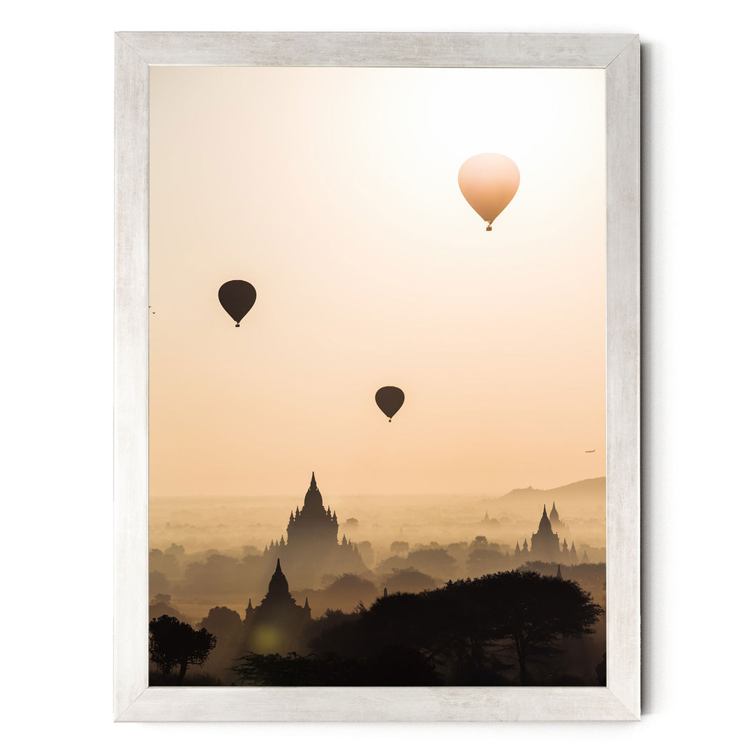 three hot air balloons floating in the sky above a cityscape with silhouetted buildings.