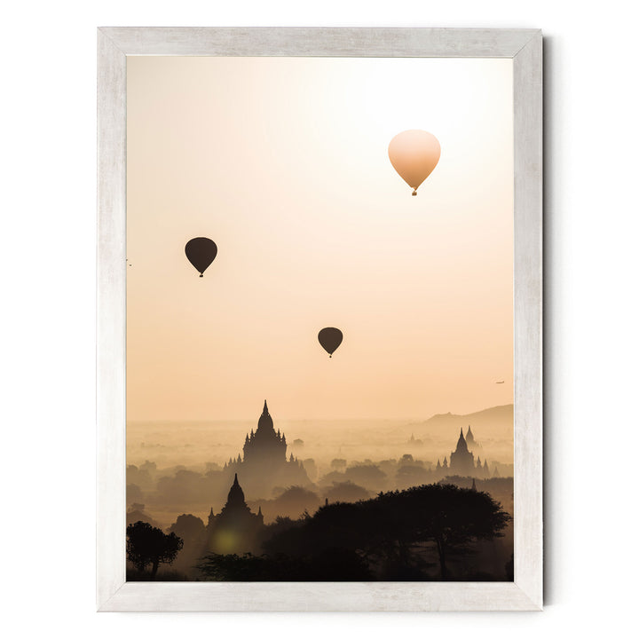 three hot air balloons floating in the sky above a cityscape with silhouetted buildings.