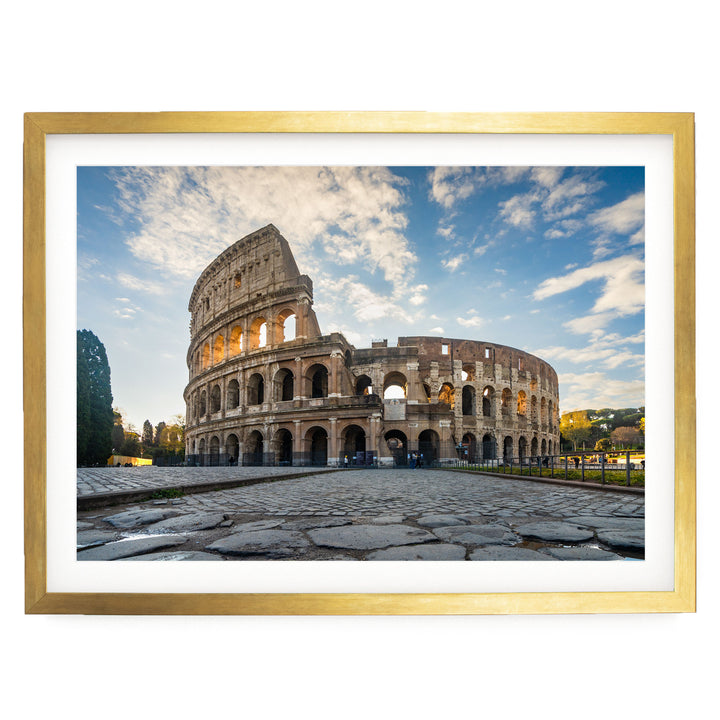 the Colosseum, a famous ancient amphitheater in Rome, Italy. The Colosseum has a distinctive oval shape and is surrounded by a stone courtyard. The sky above is blue with some clouds, creating a picturesque scene. The image is framed and appears to be a photograph of the Colosseum.