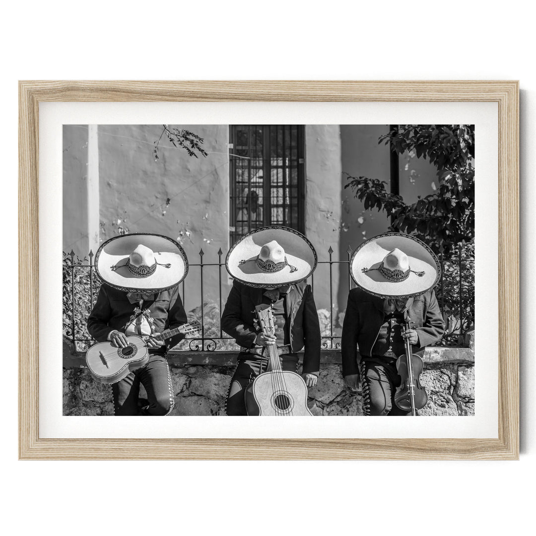 Three musicians wearing sombreros and playing guitar and maracas, arranged in a row, with a stone wall and window in the background.