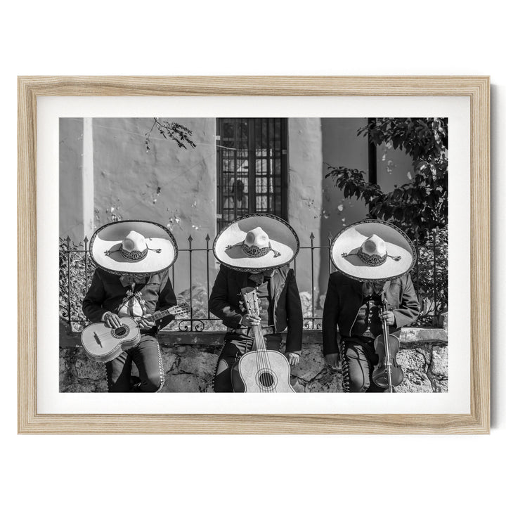 Three musicians wearing sombreros and playing guitar and maracas, arranged in a row, with a stone wall and window in the background.