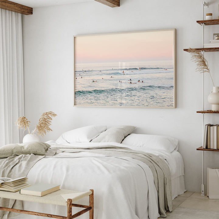 a serene bedroom scene with a large framed picture of a beach scene hanging on the wall above a bed with white linens and a gray throw blanket.