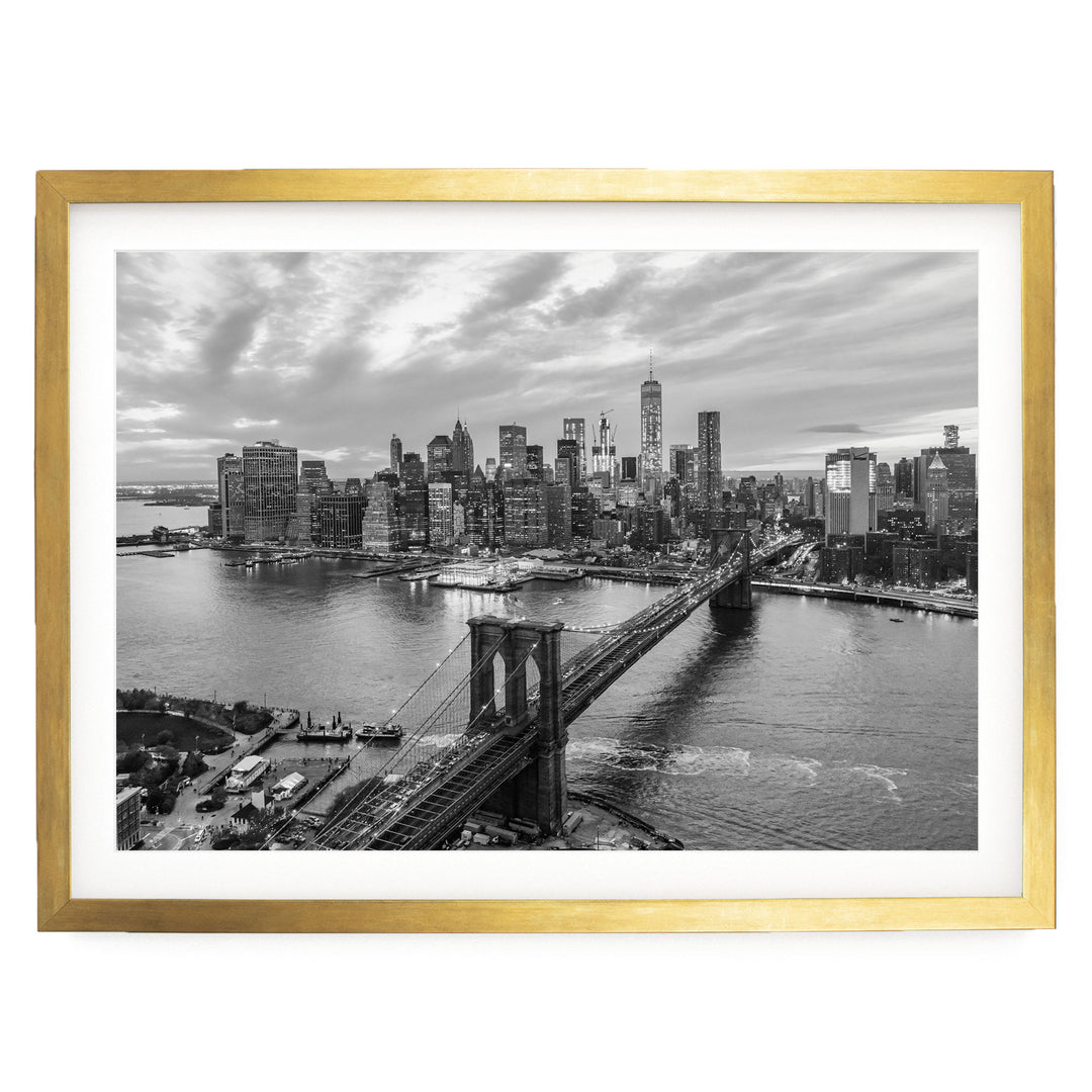 A black and white aerial view of the New York City skyline, featuring the Brooklyn Bridge and the surrounding cityscape.