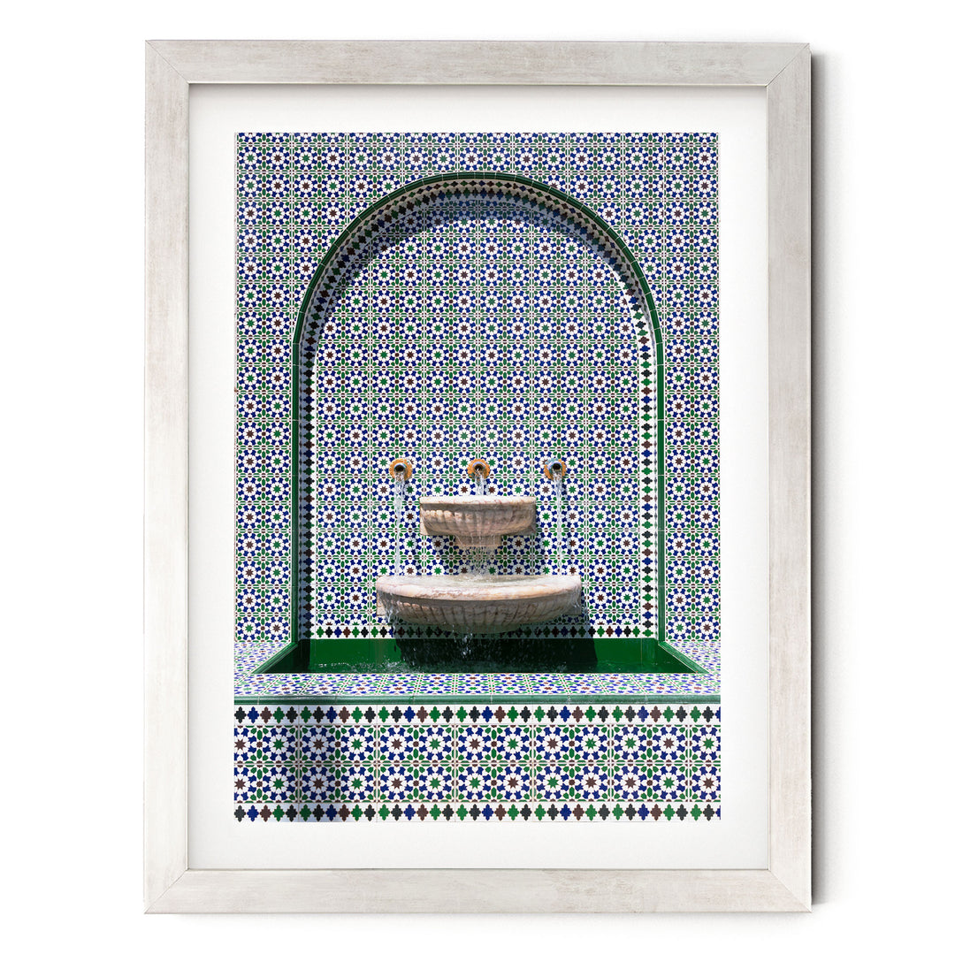 a white-framed picture of a fountain with a green and blue tile pattern surrounding it.