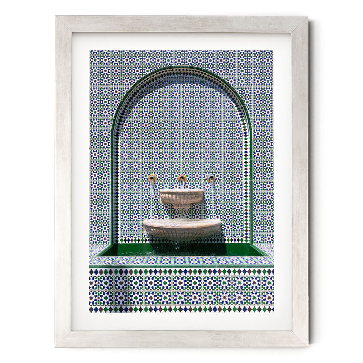 a white-framed picture of a fountain with a green and blue tile pattern surrounding it.