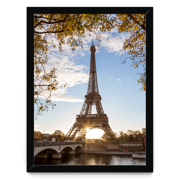the Eiffel Tower in Paris, France, with a bridge and trees in the foreground, and the sun setting behind the tower.