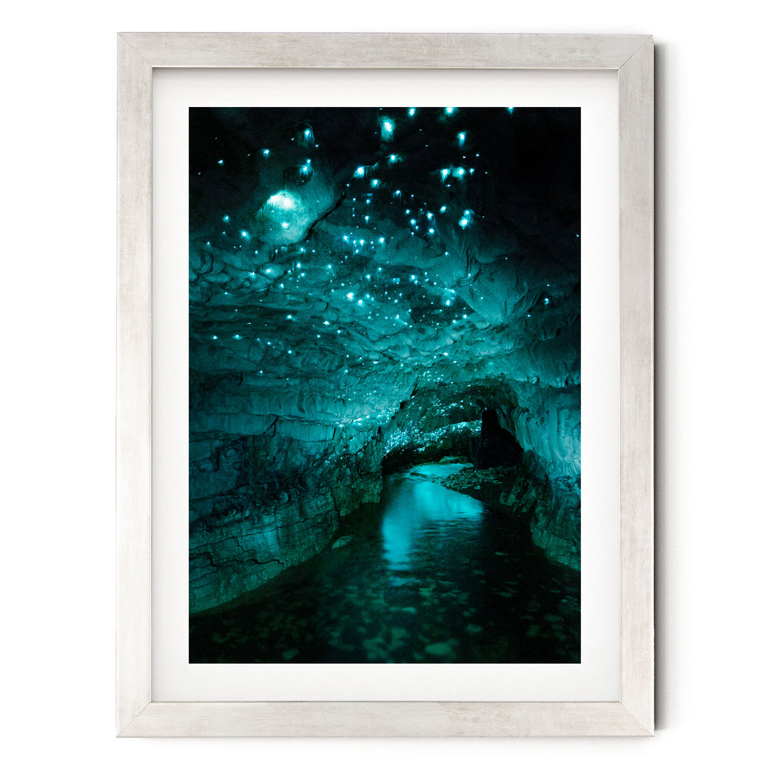 A framed photograph depicting a cave with a stream of water flowing through it, surrounded by glowing blue lights that create a mesmerizing, otherworldly atmosphere.
