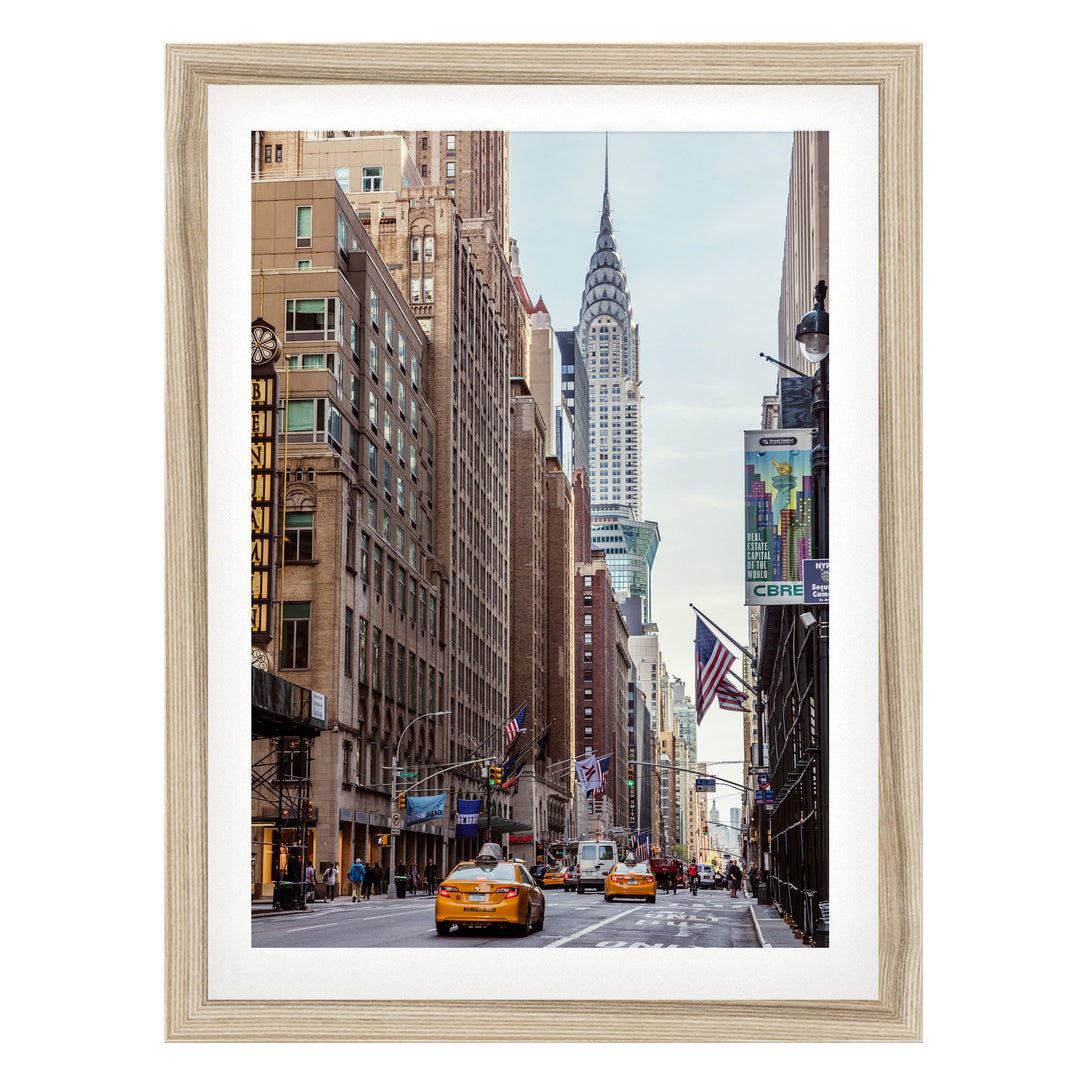 A busy city street with tall buildings, including the iconic Chrysler Building, and yellow taxis driving down the road.