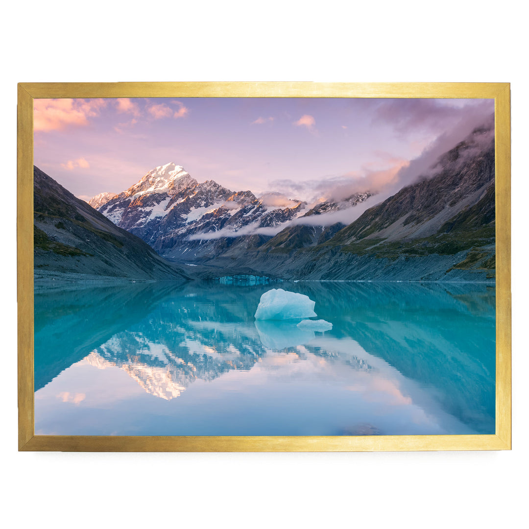 A breathtaking landscape featuring a serene lake with a large ice formation in the center, surrounded by majestic snow-capped mountains under a vibrant sky.