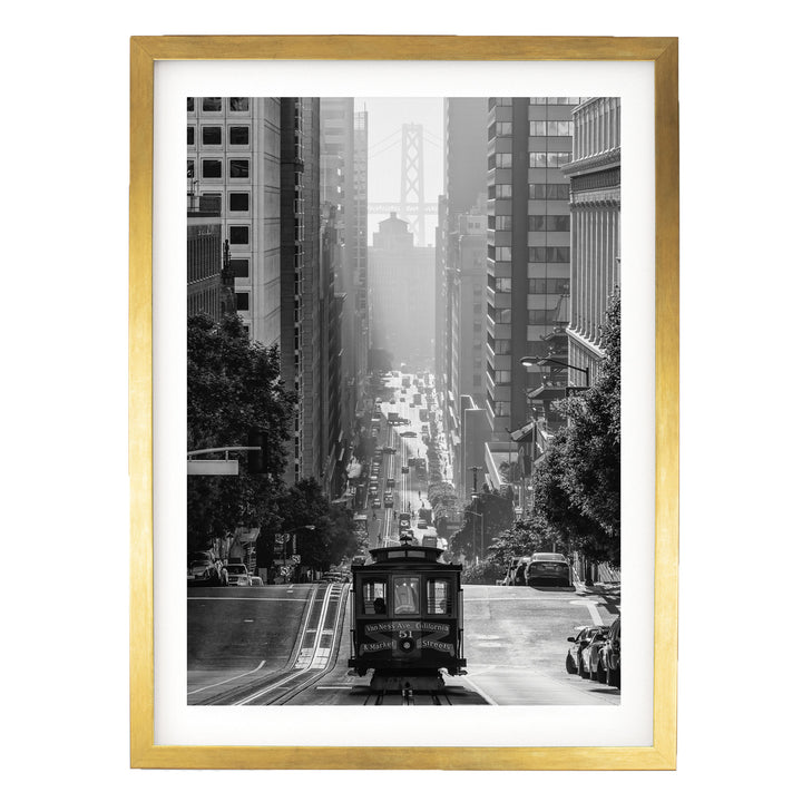 A black and white photograph of a trolley car traveling down a city street, surrounded by tall buildings and a bridge in the distance.