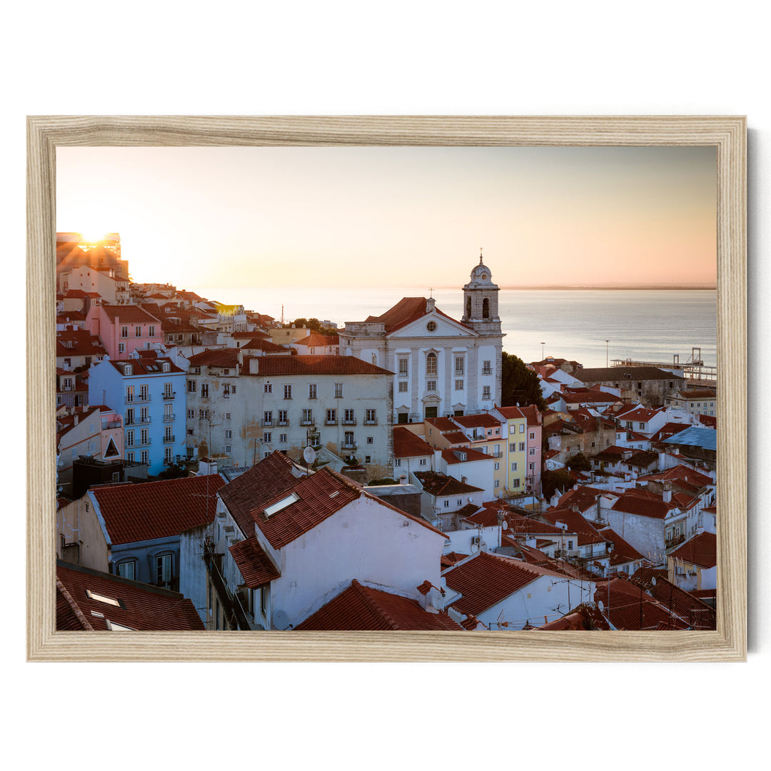 a picturesque town with a church and colorful buildings set against a backdrop of a sunset over the ocean.
