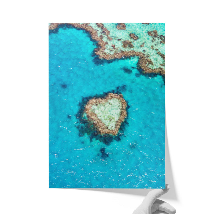 The image is a photograph of a coral reef with a heart-shaped rock formation in the center, surrounded by the vibrant blue ocean.