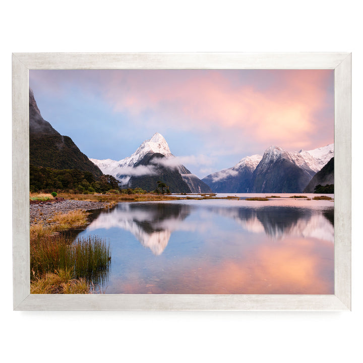 a serene landscape with a calm lake reflecting the surrounding mountains and sky. The mountains are covered in snow, and the sky is a beautiful gradient of pink and orange, creating a stunning backdrop for the scene.