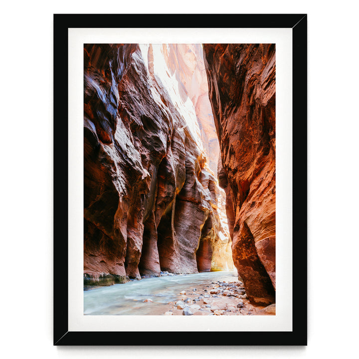 A framed photograph depicting a narrow, winding river flowing through a canyon with towering red rock walls on either side.