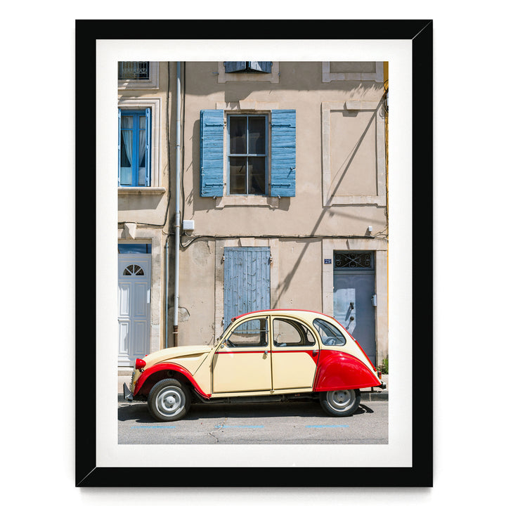 A vintage red and cream-colored car is parked on a street in front of a building with blue shutters and a white door.