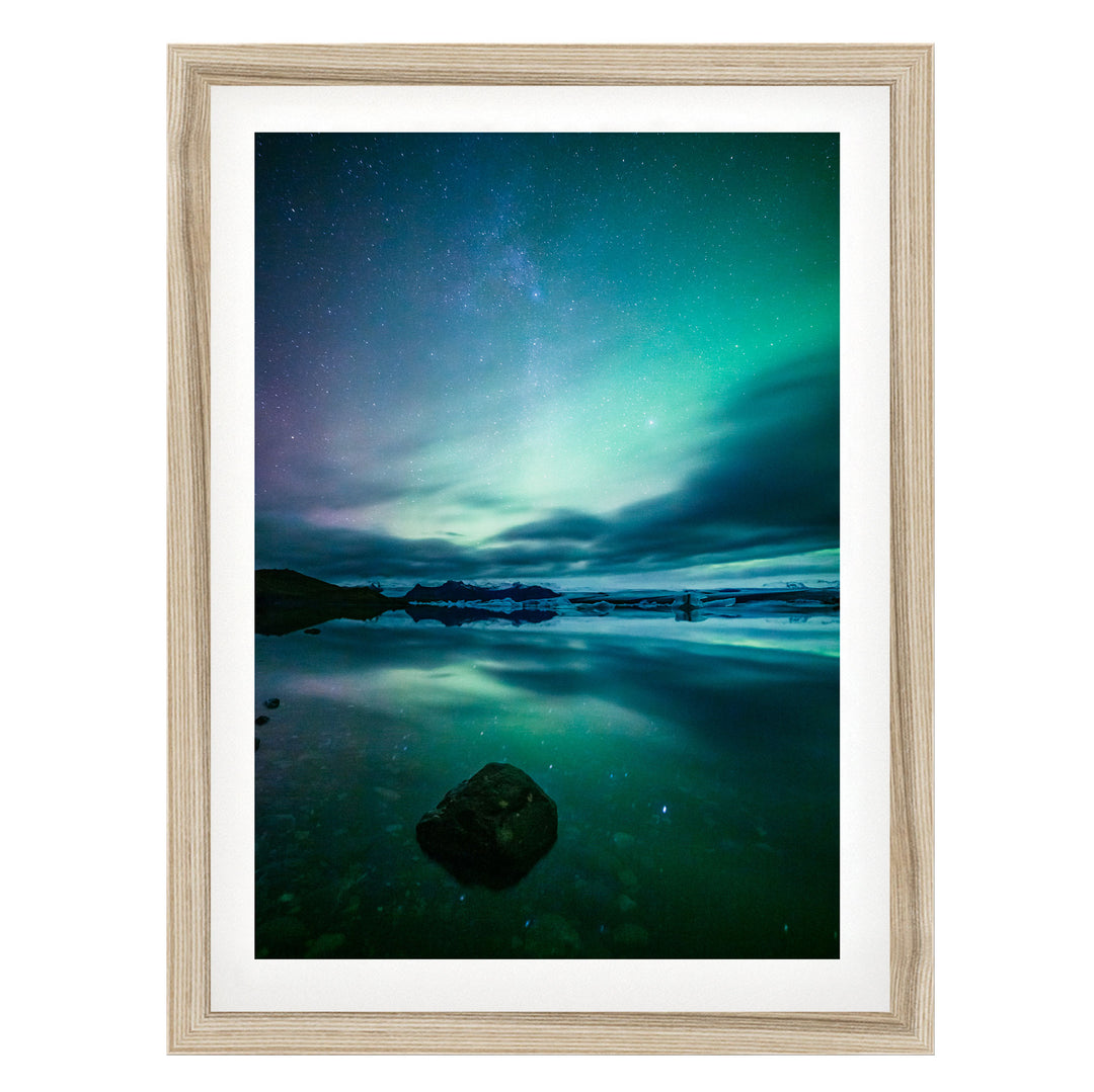 a serene night scene with a calm body of water reflecting the vibrant colors of the night sky, including shades of blue, green, and purple.