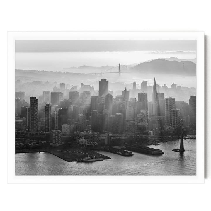 A black and white aerial view of a densely populated city skyline, with the Golden Gate Bridge and foggy mountains in the background.