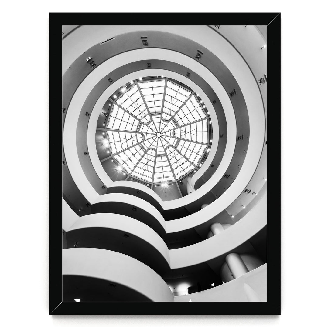 A black and white photograph of a spiral staircase with a large circular skylight at the top, creating a striking architectural feature.