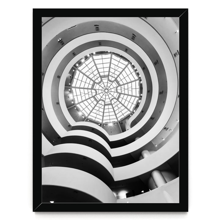 A black and white photograph of a spiral staircase with a large circular skylight at the top, creating a striking architectural feature.