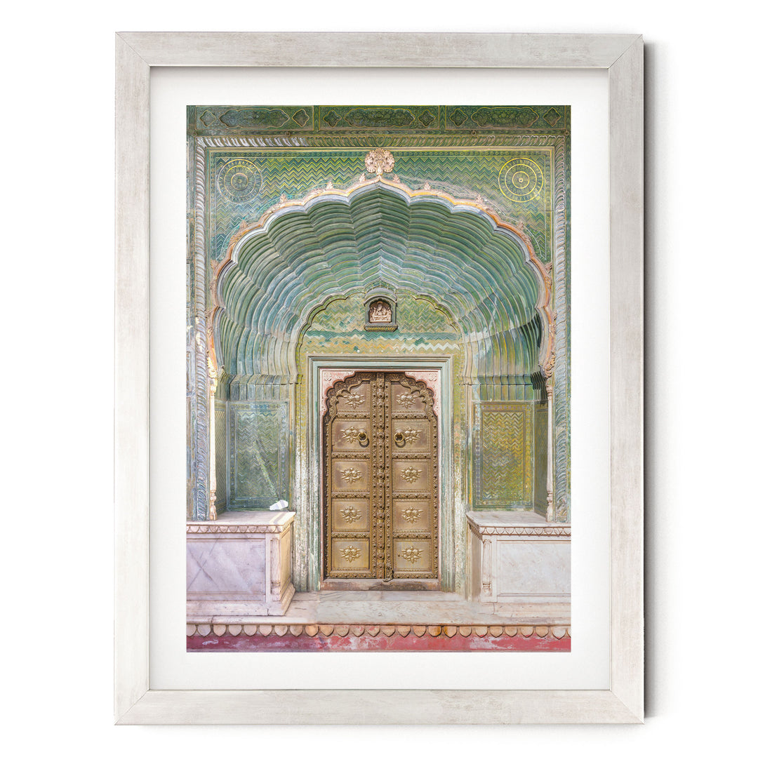 a large, ornate wooden door with intricate carvings and a colorful, patterned archway above it. The door is set into a white marble wall, creating a striking contrast between the natural and man-made elements. The frame surrounding the door is white, which further accentuates the vibrant colors and detailed carvings of the door.