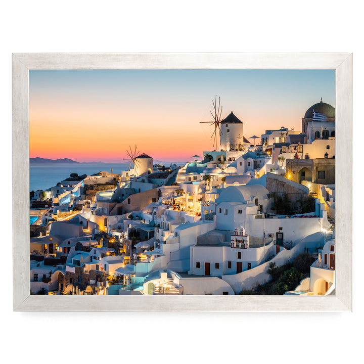 a picturesque coastal town with white buildings and windmills, set against a stunning sunset sky.