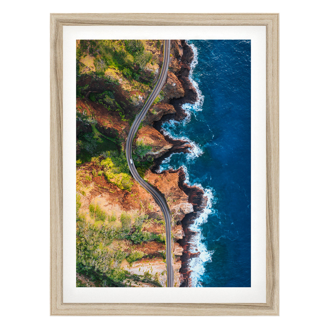 The image is an aerial view of a winding road cutting through a rugged coastline with cliffs and the ocean.