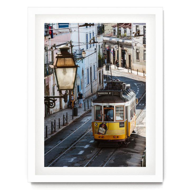 A yellow tram is traveling down a street lined with buildings and lampposts.