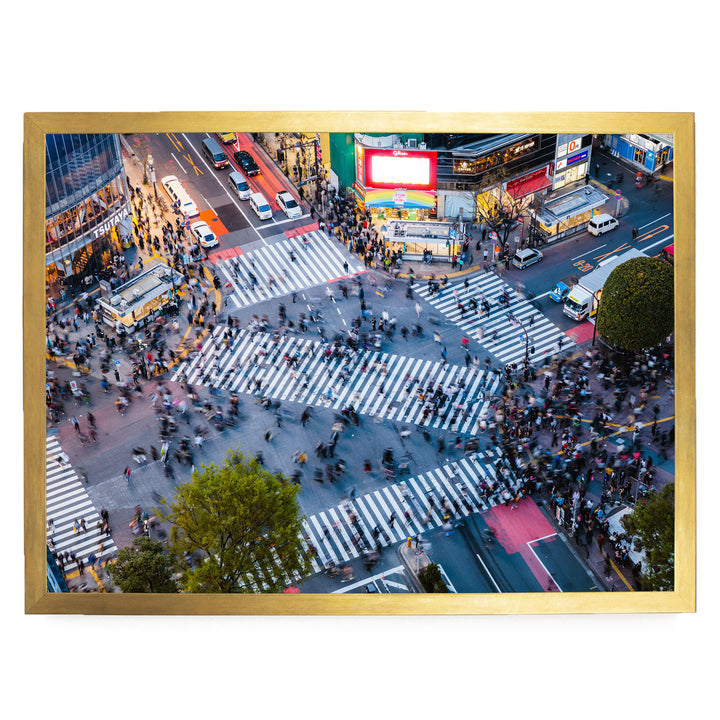 a busy city intersection with a large crowd of people crossing the street, surrounded by tall buildings and illuminated by bright lights.