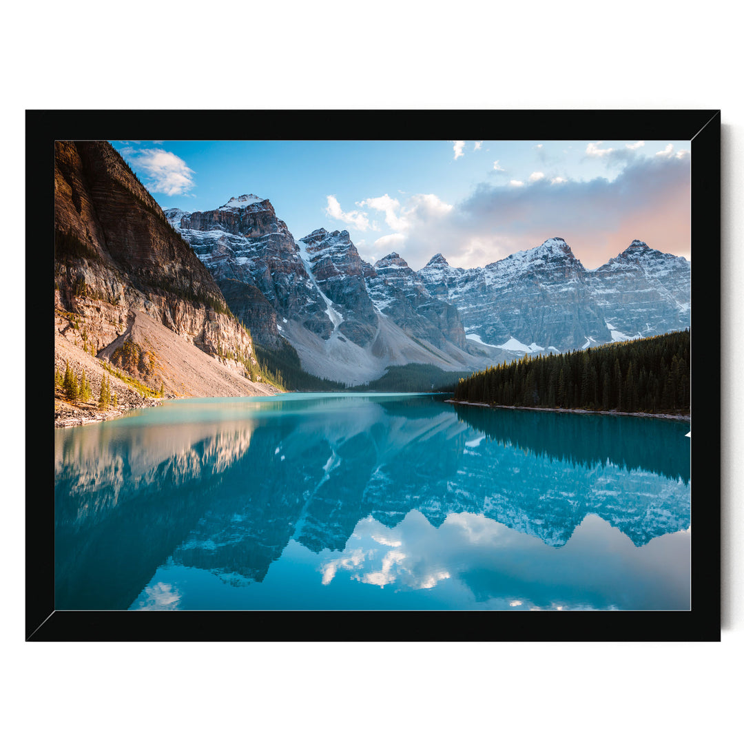 A breathtaking view of a serene mountain lake, with the mountains reflected perfectly in the calm waters. The sky above is a beautiful shade of blue, dotted with a few clouds, creating a picturesque scene. The image is framed, adding a touch of elegance to the overall composition.