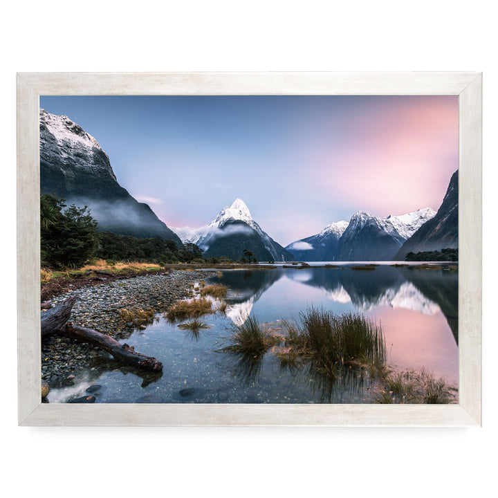 a serene mountain landscape with snow-capped peaks reflected in a calm lake, surrounded by lush vegetation and a rocky shore.