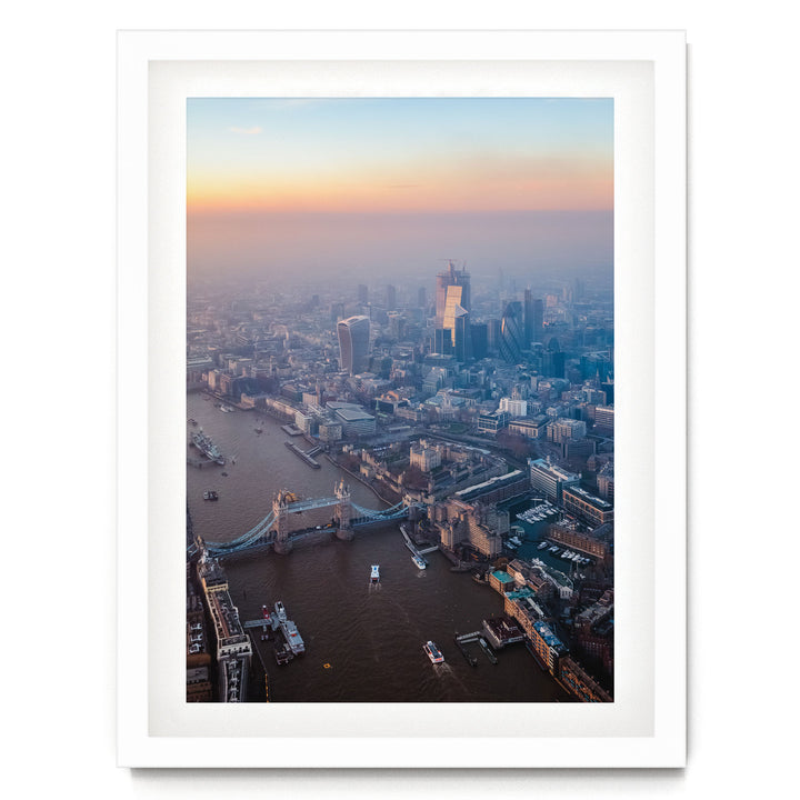The image is an aerial view of a cityscape with a river running through it, featuring a bridge and several boats. The city is densely populated with tall buildings, and the sky is filled with warm, hazy colors, suggesting a sunrise or sunset.