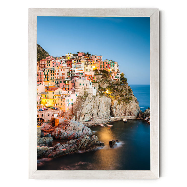 A picturesque coastal town nestled on a cliff, with its buildings painted in a variety of colors and illuminated by warm lighting, creating a vibrant and charming scene.