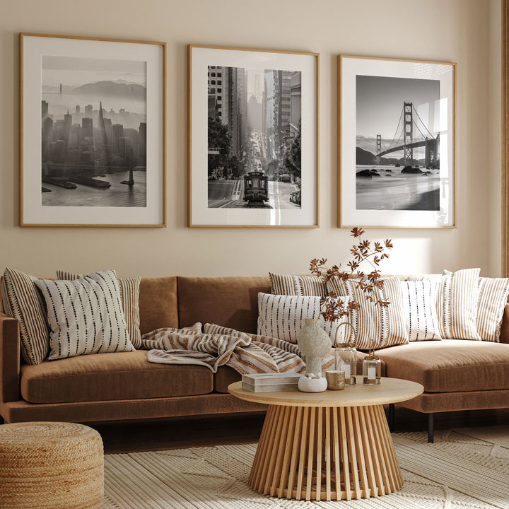 a living room with a brown sofa, a wooden coffee table, and three framed black and white photographs of cityscapes hanging on the wall above the sofa.