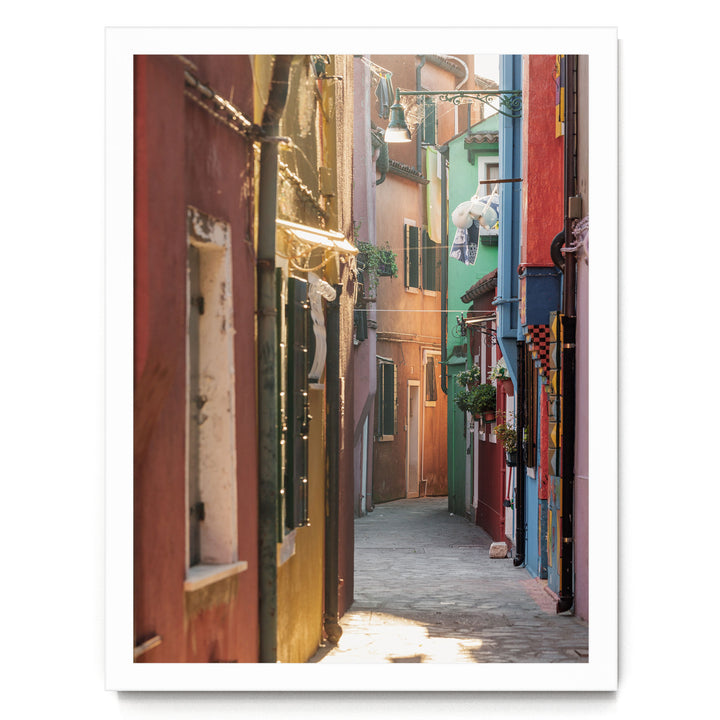 A narrow, colorful alleyway in a city, with buildings painted in various vibrant colors lining the sides. The buildings have windows and balconies, and there are plants and other decorative elements throughout the scene.