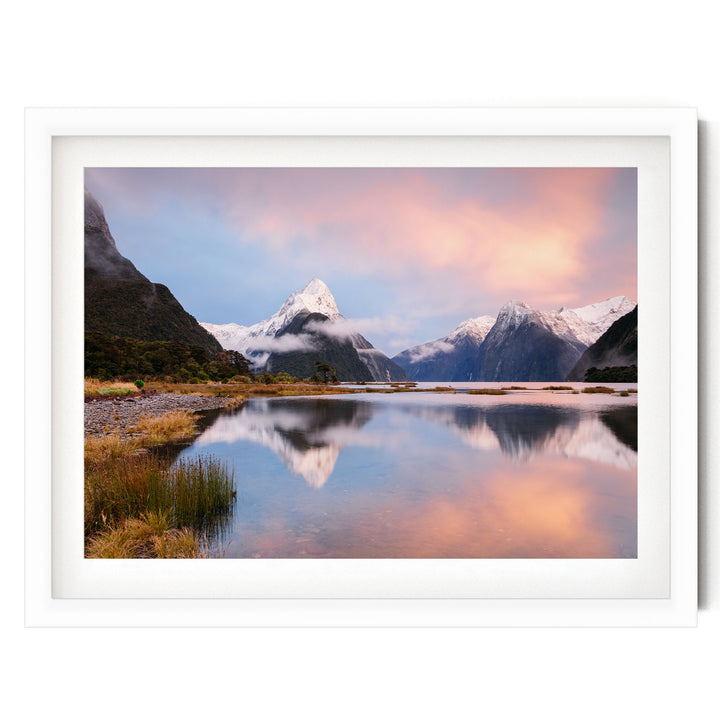 A serene landscape featuring a mountain range reflected in a calm lake, with a stunning sunset sky casting a warm glow over the scene.