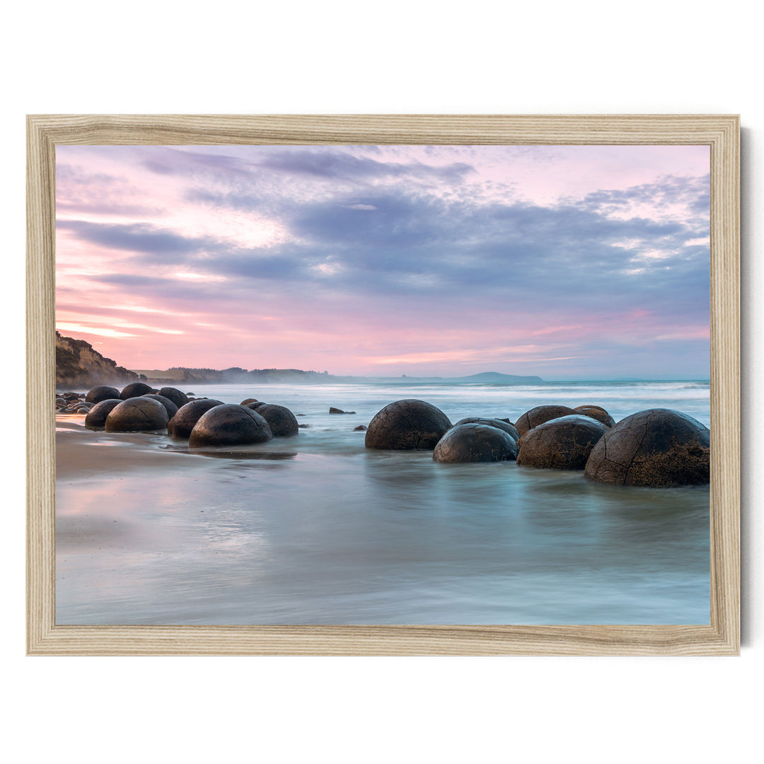 A serene beach scene with a collection of large, round boulders in the water, set against a backdrop of a colorful sunset sky.