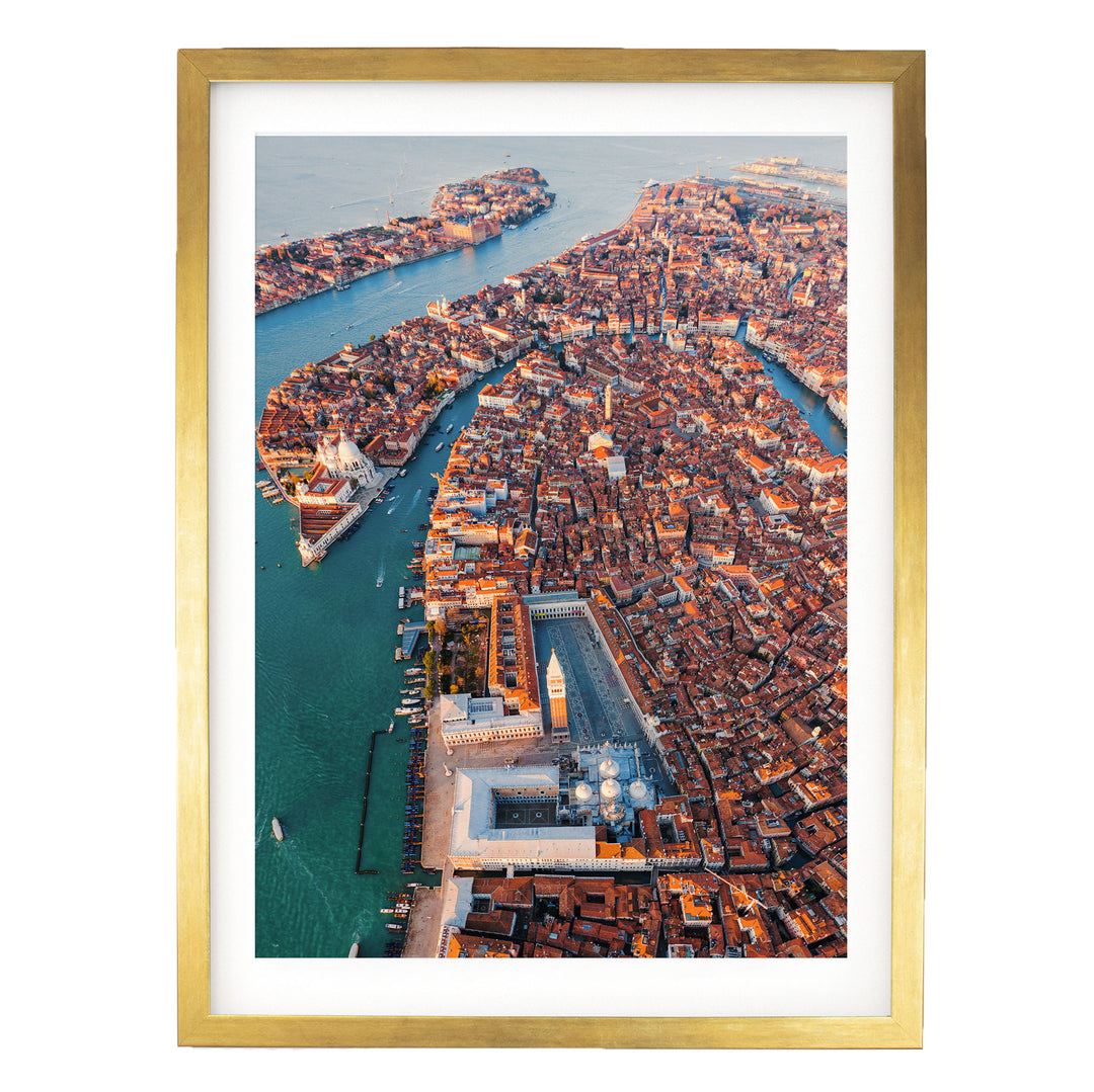 The image is an aerial view of a densely populated city with a river running through it. The city is characterized by a mix of old and new buildings, with a large white building prominently visible in the center. The surrounding waterway is filled with boats, indicating a bustling maritime activity. The image is framed in a gold frame, adding a touch of elegance to the overall composition.
