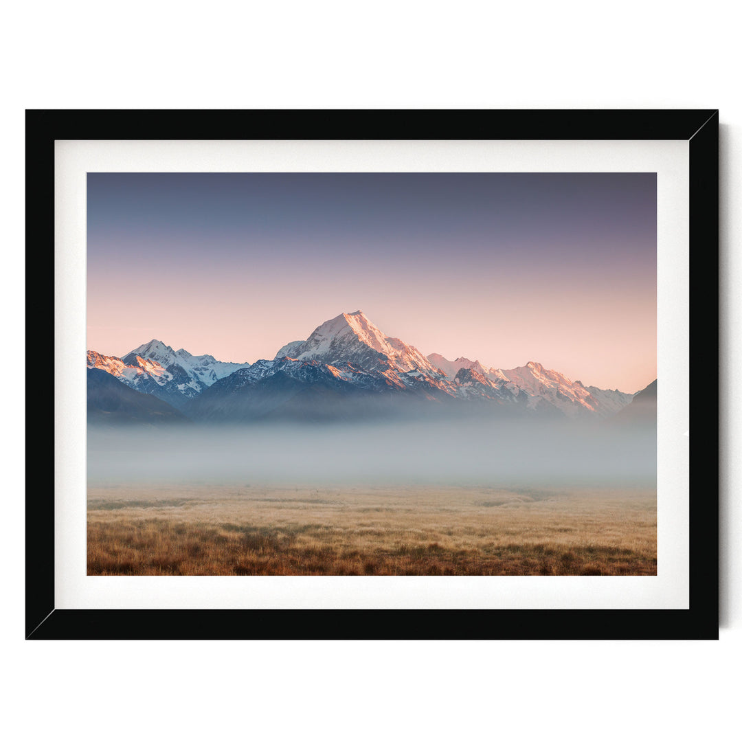 A framed image depicting a breathtaking mountain landscape with snow-capped peaks against a vibrant sky, partially obscured by a hazy mist.