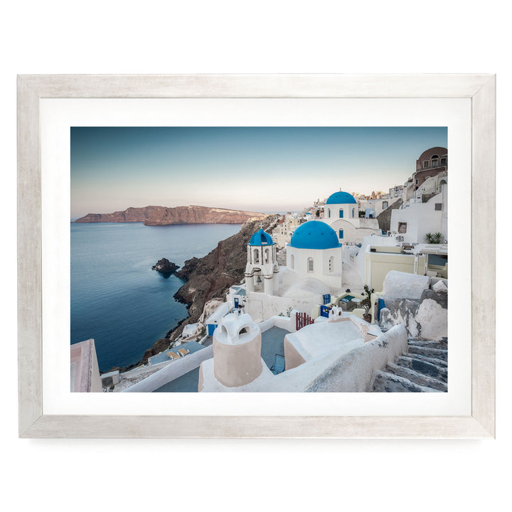 a picturesque coastal town with white buildings and blue domes overlooking the ocean.