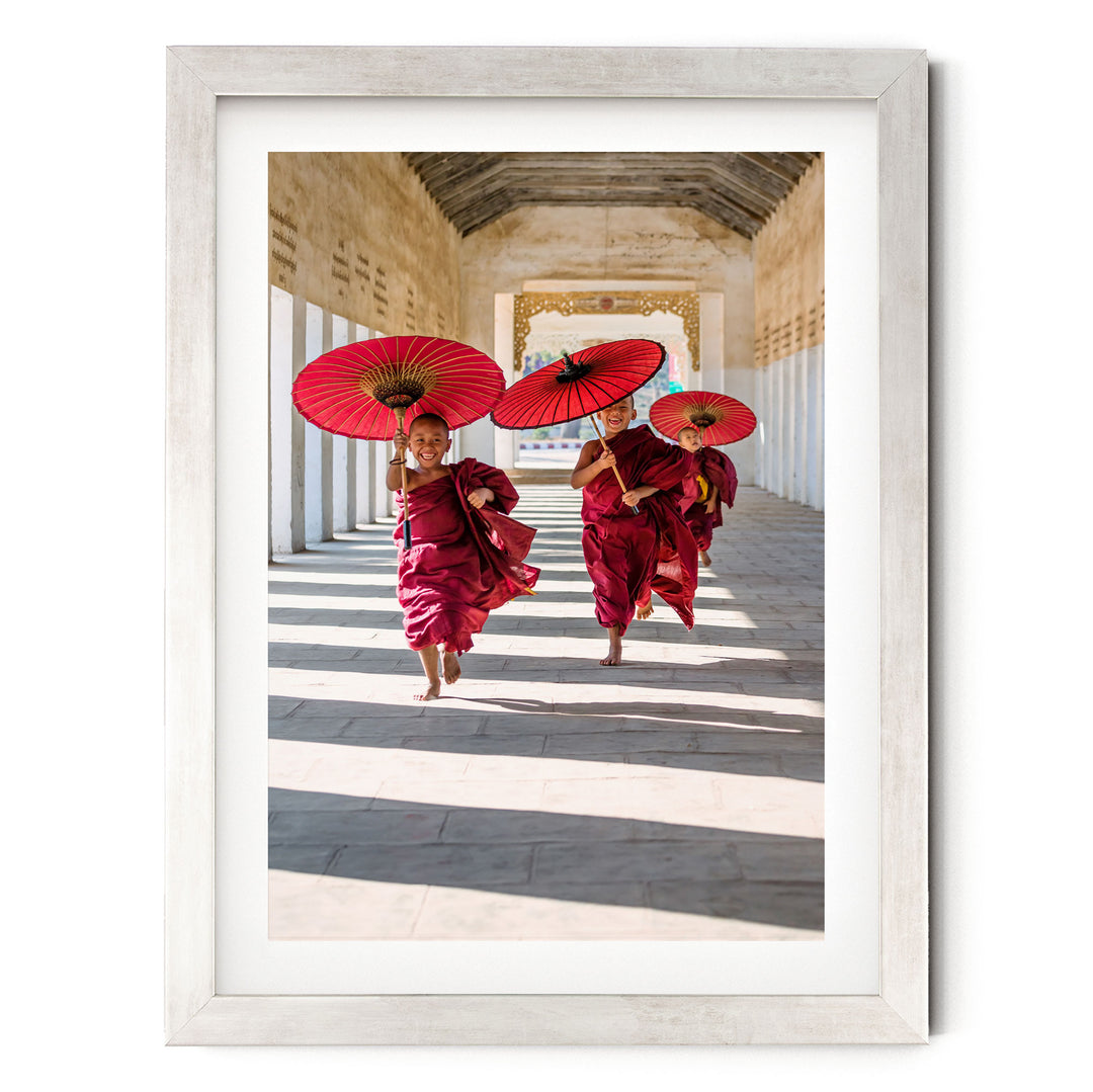 A framed photograph of two monks in red robes walking down a hallway, each holding a red umbrella.