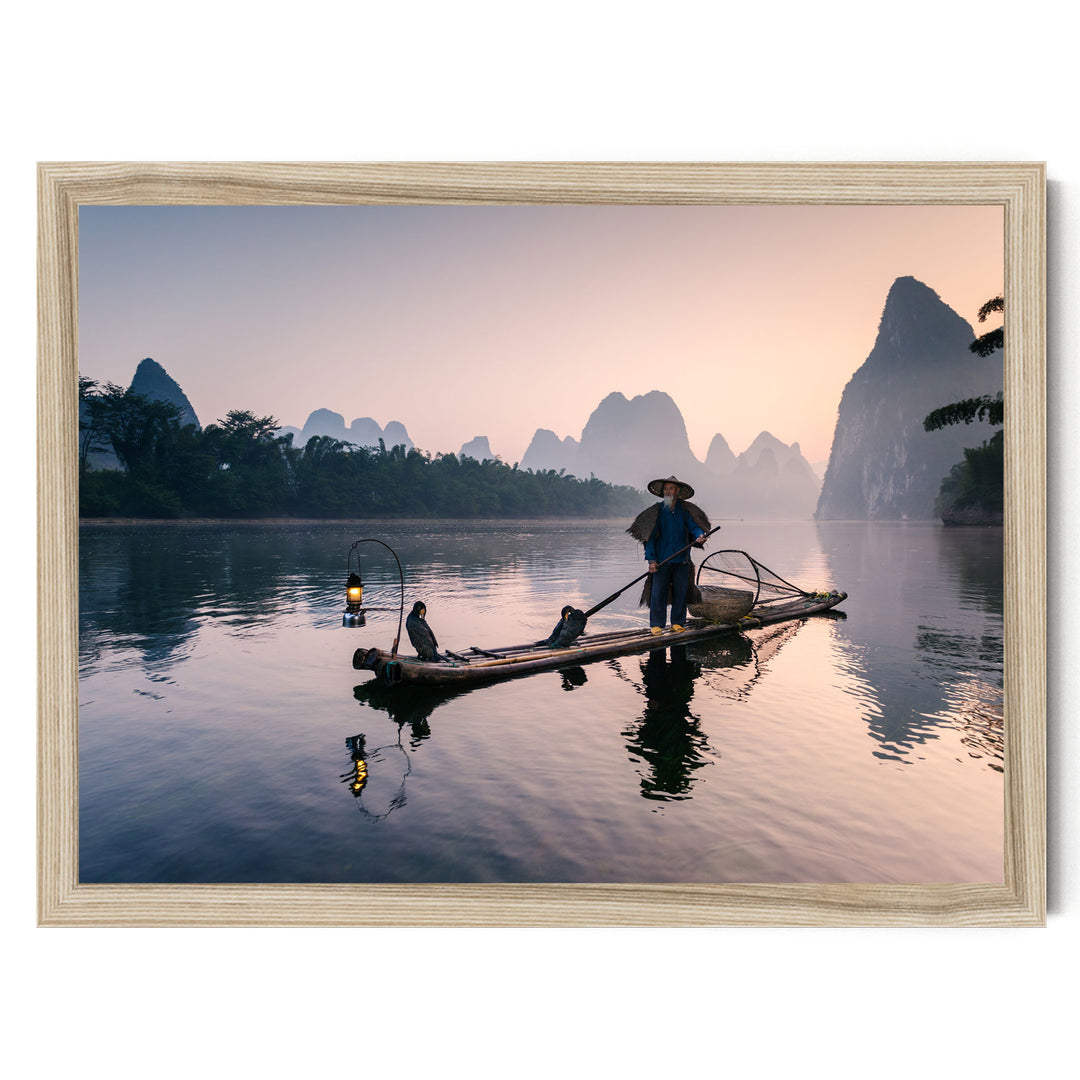 A person in a blue shirt and hat is standing on a long wooden boat, paddling through a serene lake at sunset. The boat is surrounded by lush greenery, and the sky is filled with warm hues of orange and pink, creating a picturesque scene.