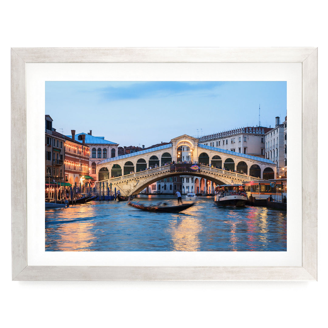 a picturesque scene of the Rialto Bridge in Venice, Italy, with its distinctive arches and lights reflecting on the water below. The bridge is surrounded by colorful buildings and boats, creating a vibrant and lively atmosphere.